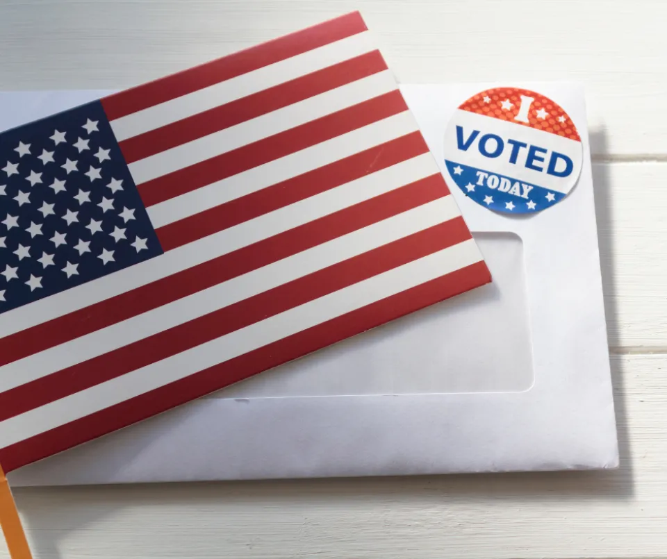 An American flag on top of an envelope with an "I Voted" sticker on it.