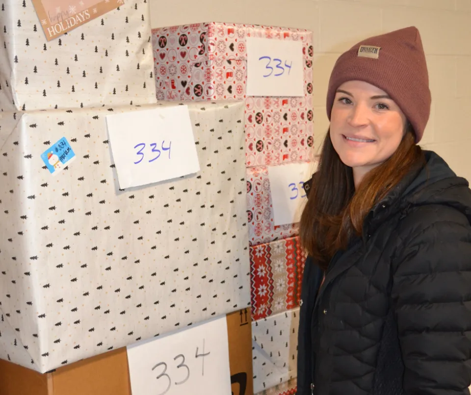 A photo of an Olmsted County employee standing next to a stack of presents that are numbered.