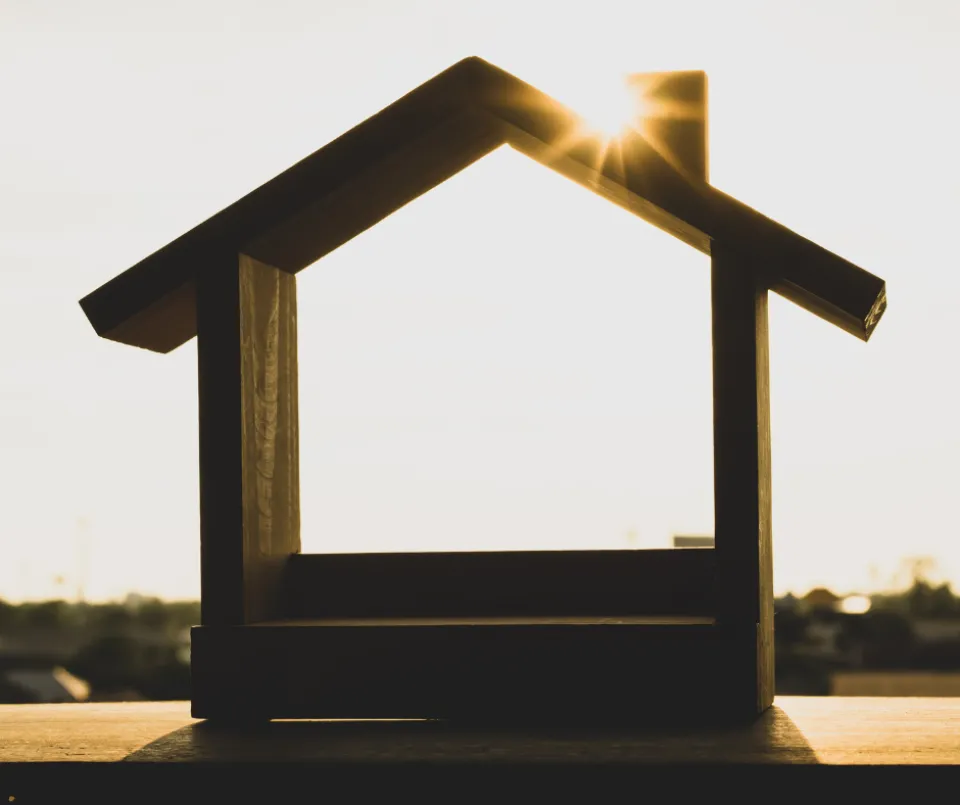 A house shape made out of wood, with the sun shining on it.