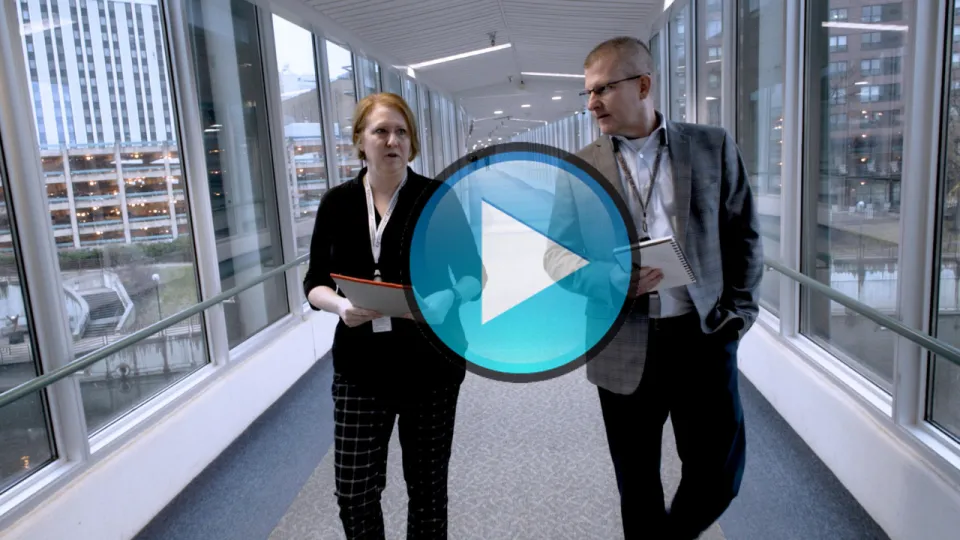 Travis Gransee walking down the skyway with a colleague. This thumbnail features a "play" button.