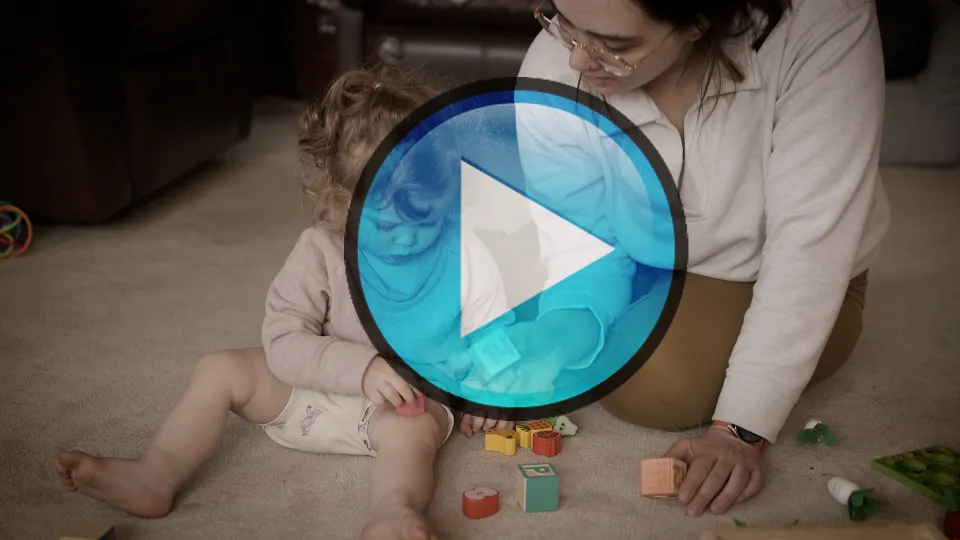 Play button over a video still of a child and her mom playing with blocks