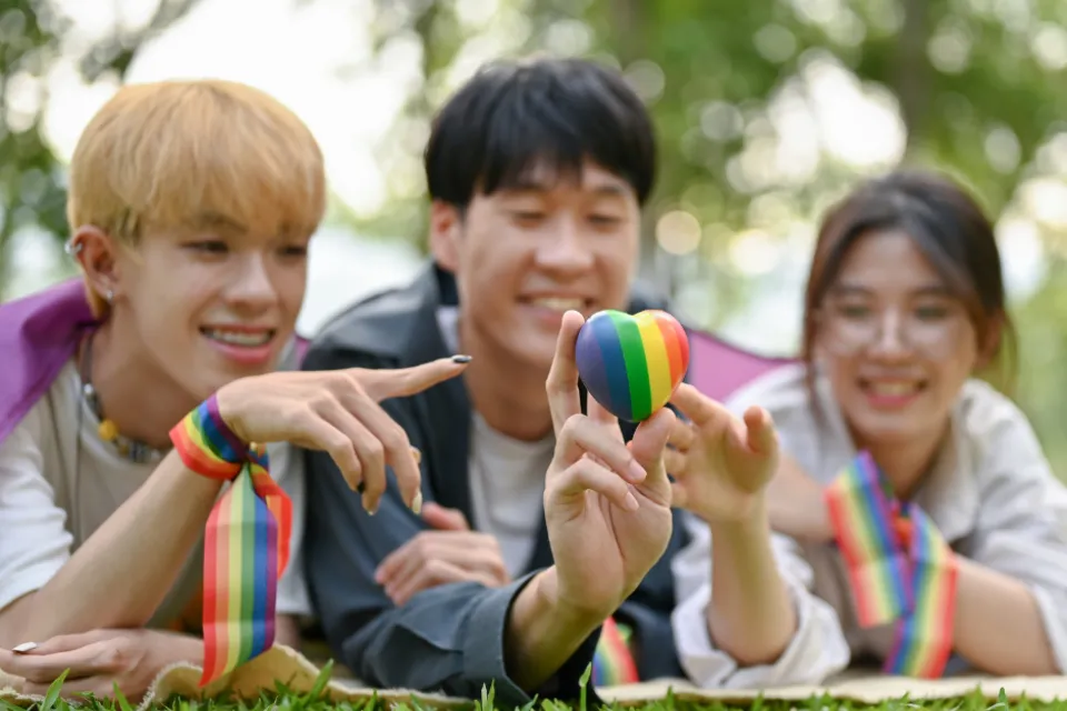 Parents holding a rainbow-colored heart while posing with their LGBT teen.