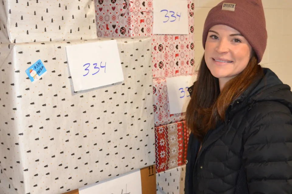 A photo of an Olmsted County employee standing next to a stack of presents that are numbered.