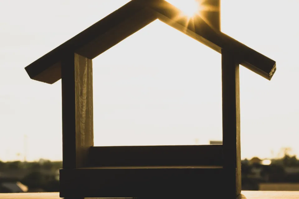 A house shape made out of wood, with the sun shining on it.