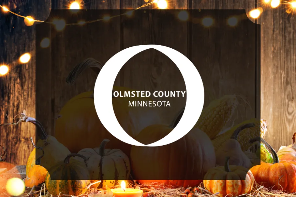 Olmsted County logo. A festive fall scene behind the logo with pumpkins and twinkle lights.