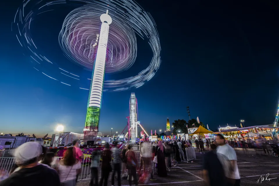 A picture of a carnival ride spinning at the Olmsted County Fair. People watching from below.