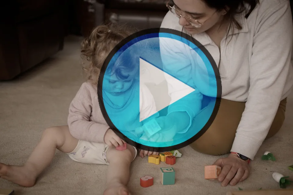 Play button over a video still of a child and her mom playing with blocks